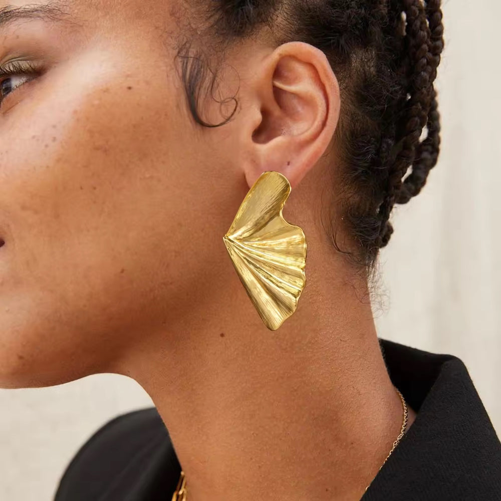 Close-up of a person wearing a gold earring with a neutral background