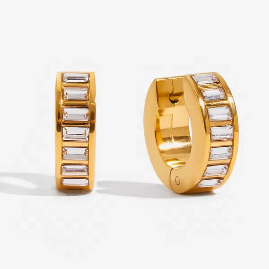 A pair of gold huggie hoop earrings with baguette-cut clear stones, shown from two angles on a light gray background.