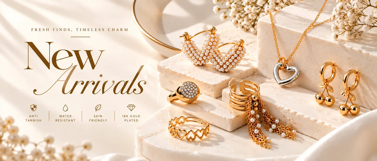 A styled jewelry display featuring gold and silver-toned rings, necklaces, earrings, and pearl accents arranged on white marble blocks with dried flowers. Large text on the left reads 'New Arrivals' with smaller marketing copy above.