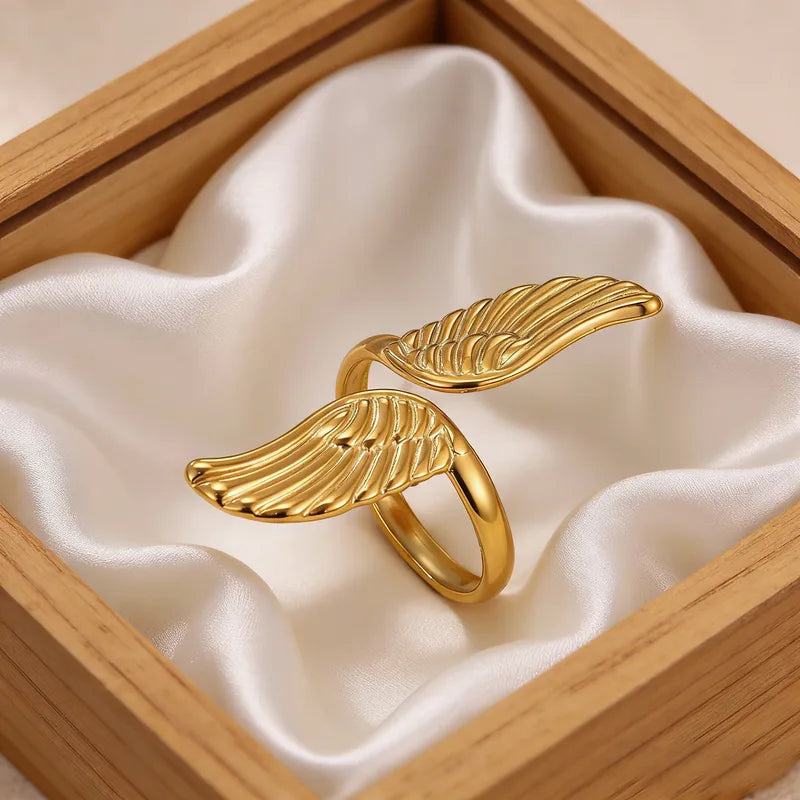 Gold wing-shaped ring on white fabric inside a wooden box