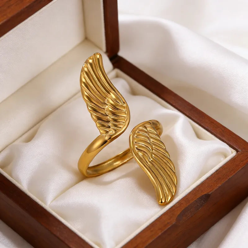 A gold wing-shaped ring displayed inside an open wooden jewelry box with cream satin lining.