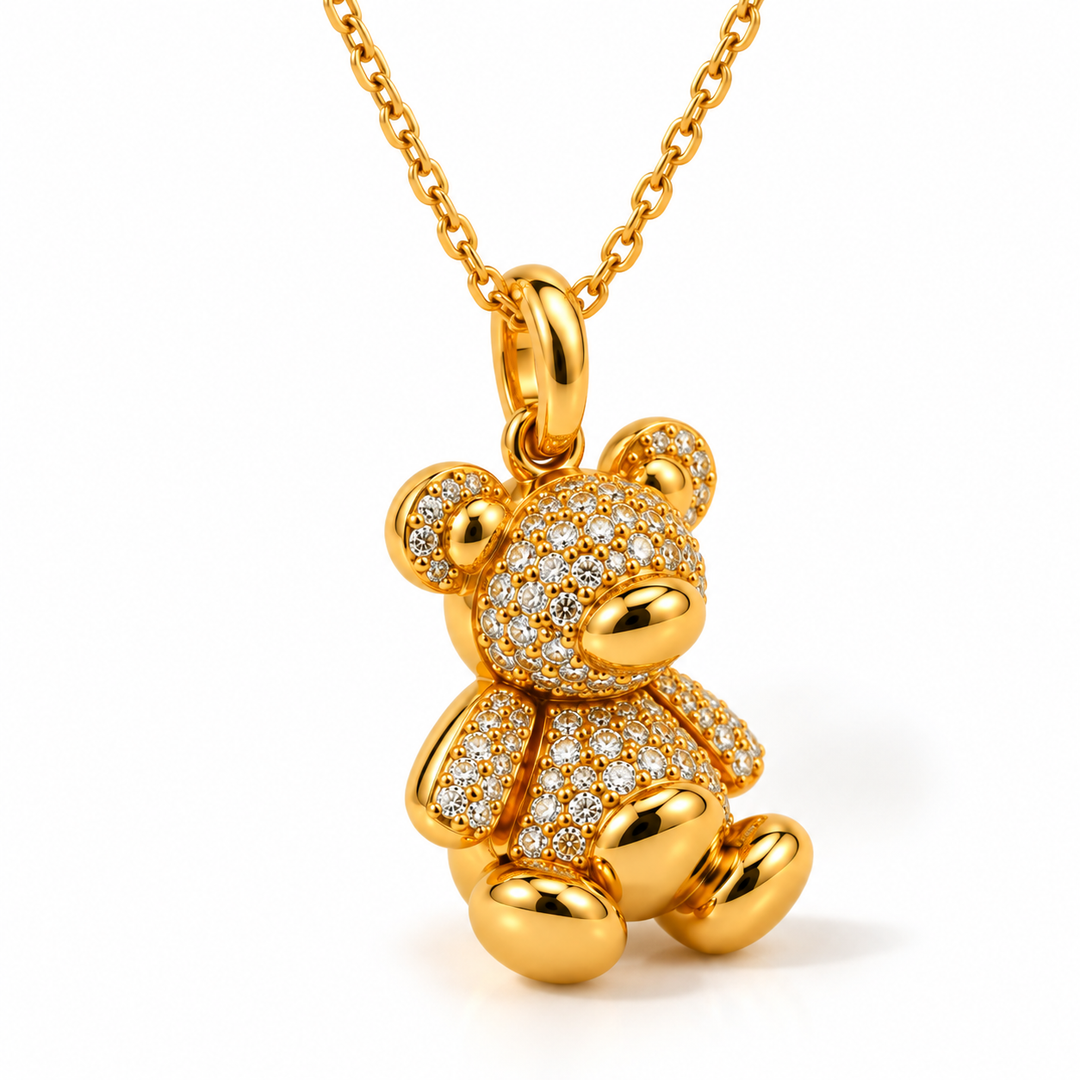 A gold teddy bear pendant necklace paved with small clear stones, shown on a white background with a gold chain.