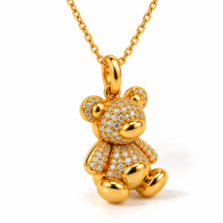 A gold teddy bear pendant necklace paved with small clear stones, shown on a white background with a gold chain.