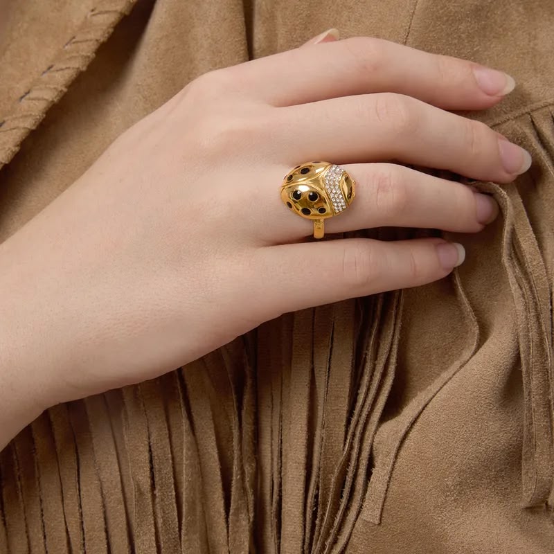 Gold ring with black gemstones on a hand against a brown textured fabric background
