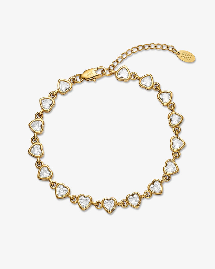 A gold heart-link bracelet with clear crystal accents, a lobster clasp, and an adjustable chain extender with a small tag, shown on a light gray background.