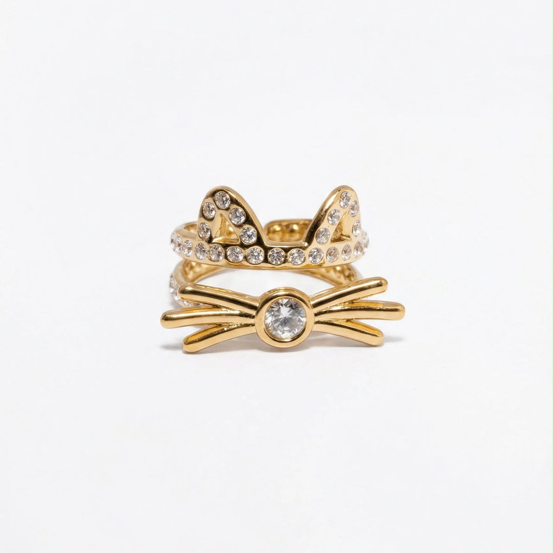 A gold cat-themed ring set featuring a bow with a central clear crystal and two cat ears studded with small clear crystals, shown on a plain white background.