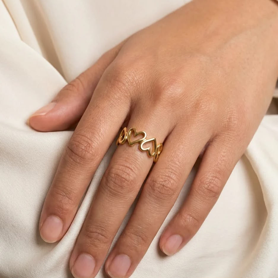A gold ring with three interlocking open heart shapes worn on a person&