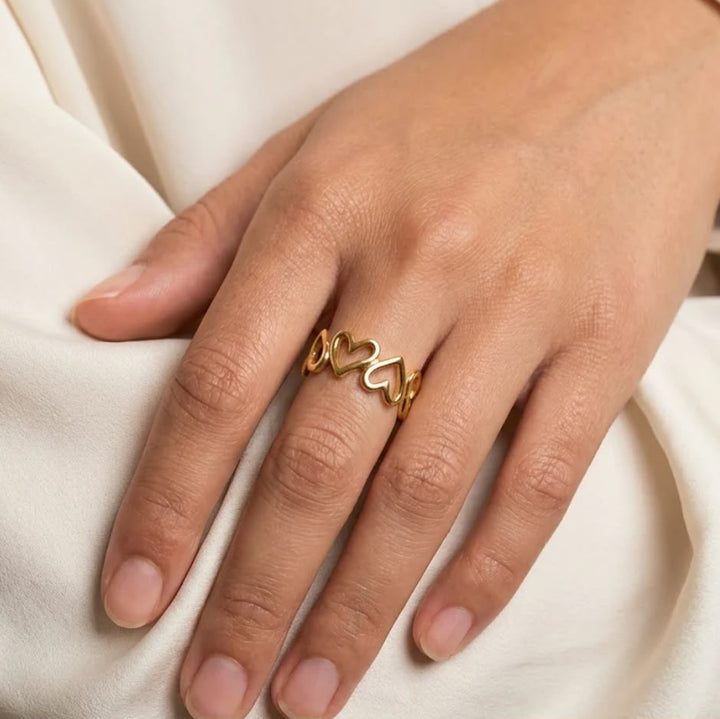 A gold ring with three interlocking open heart shapes worn on a person&