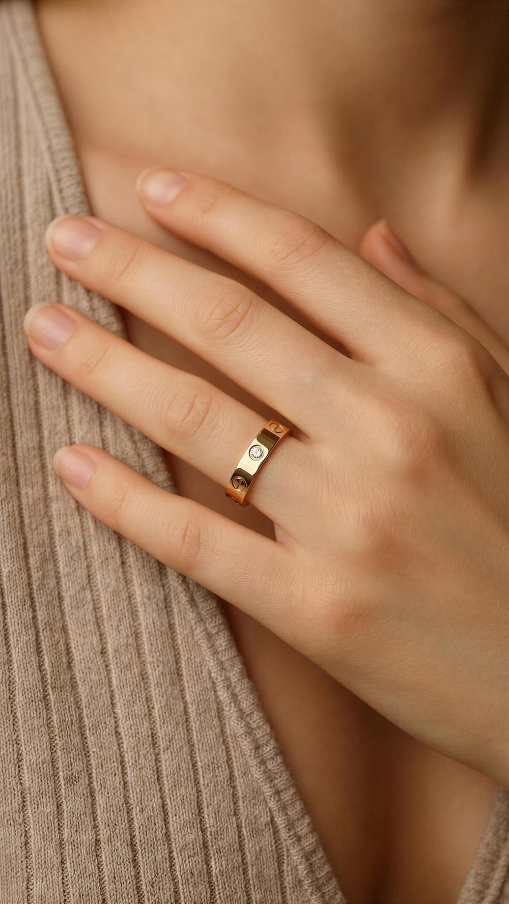 Close-up of a hand wearing a gold ring with a diamond on a beige background