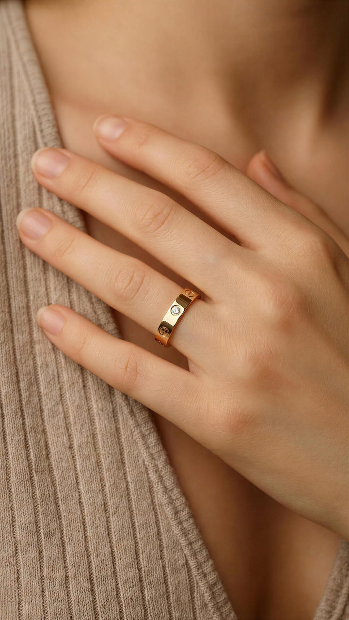 Close-up of a hand wearing a gold ring with a diamond on a beige background