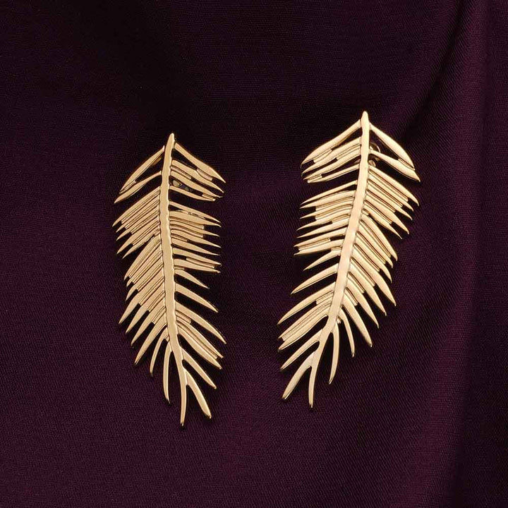 Gold leaf-shaped earrings on a dark purple fabric background