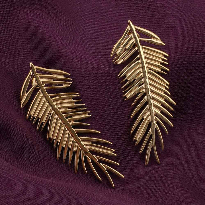 Gold leaf-shaped earrings on a purple fabric background