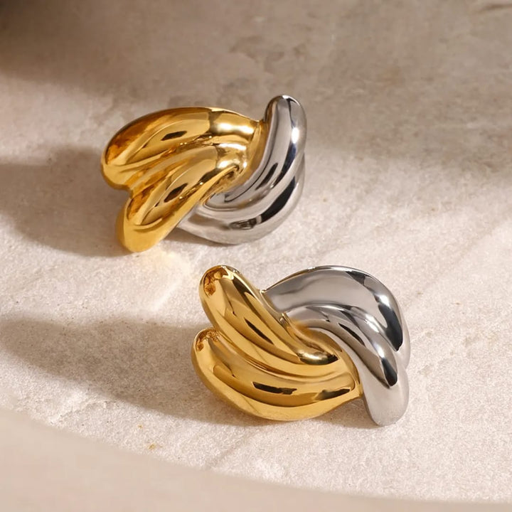Pair of gold and silver wing-shaped earrings on a beige surface