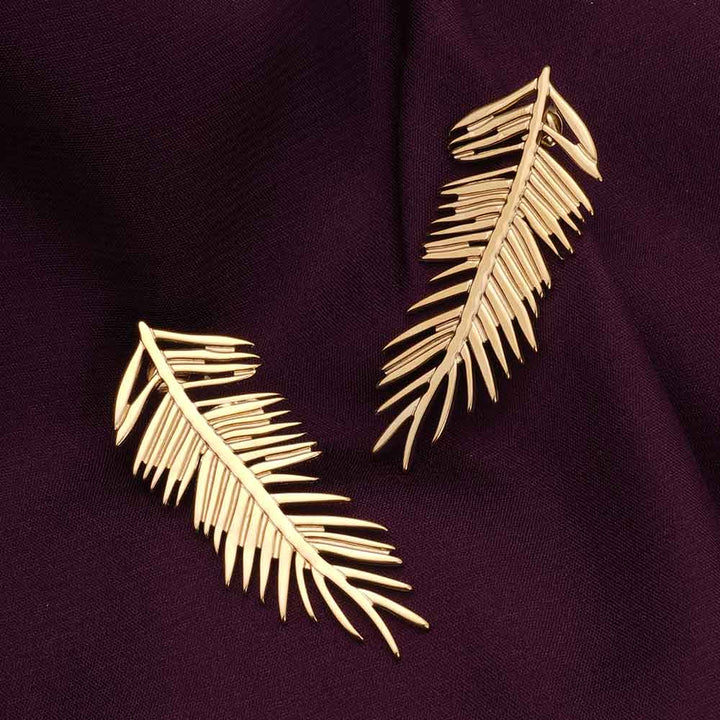 Gold leaf earrings on a dark purple fabric background