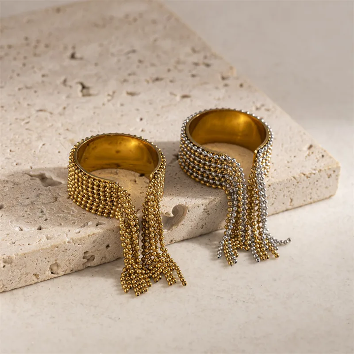 Gold bangles with fringe design on a textured stone surface