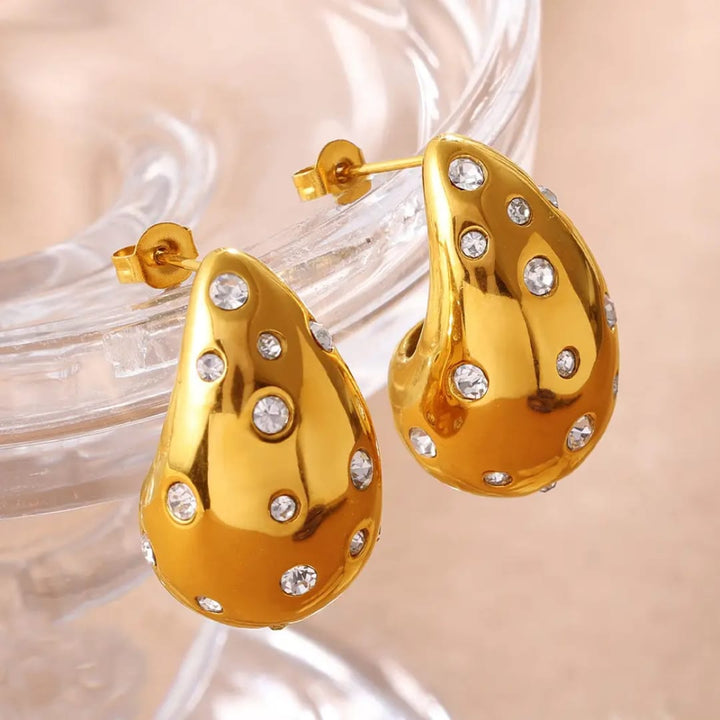 Gold earrings with clear stones on a beige background