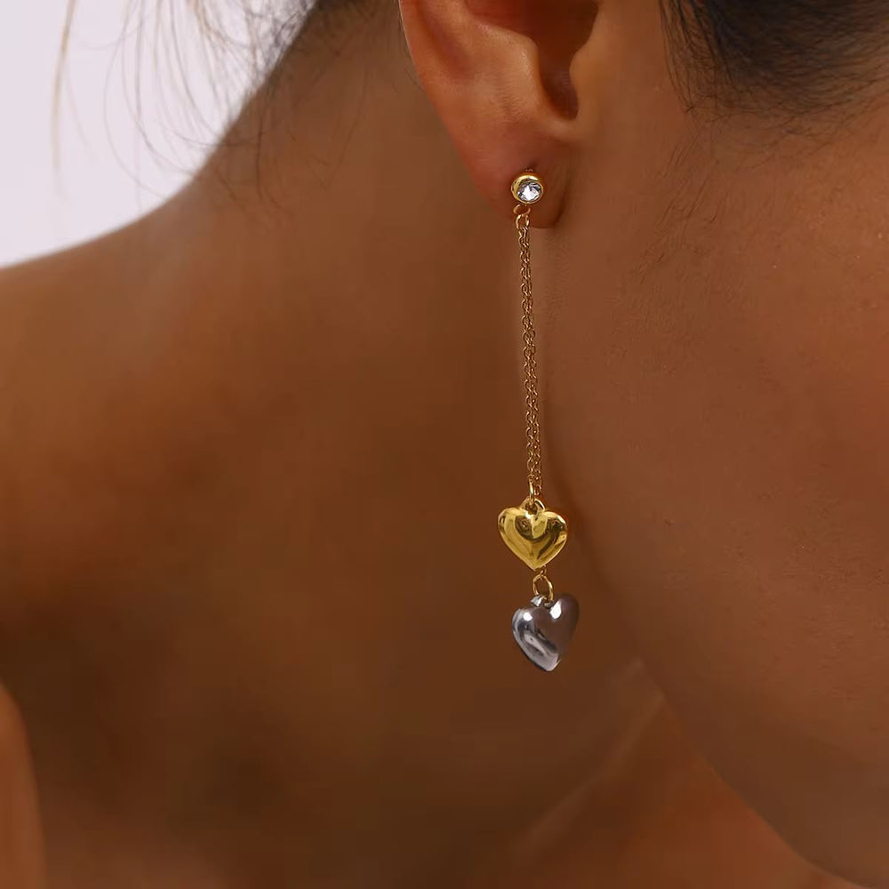 Gold chain earring with heart pendants worn by a person